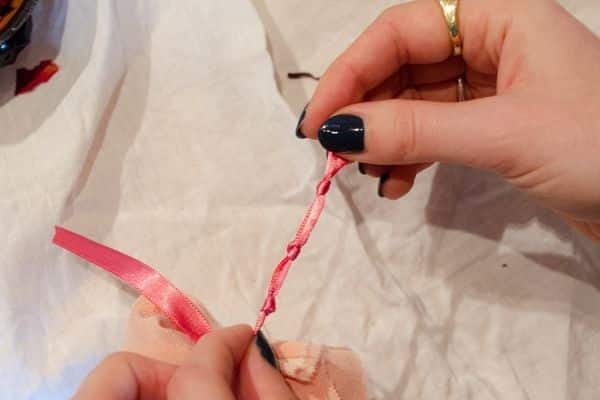 hands tying knows into pink ribbon against white linen background